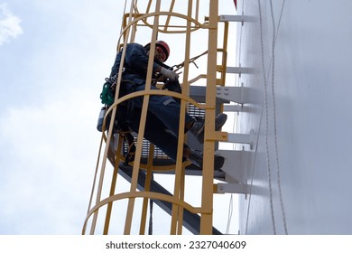 Tester man rested as he climbed a ladder to the roof of the storage tank to sprinkle it with rope. - Powered by Shutterstock