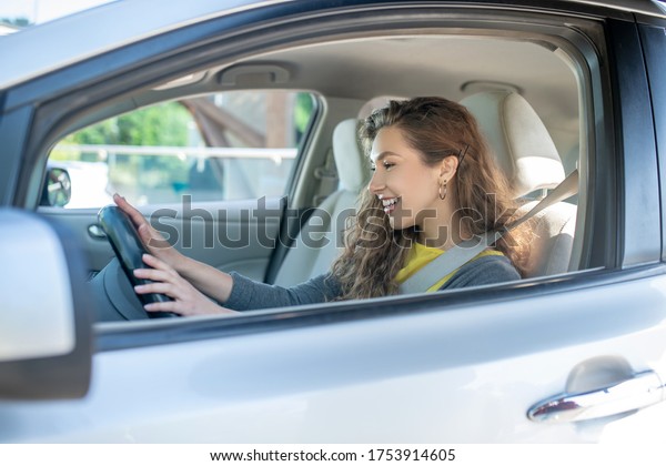 Testing new\
car. Young adult long-haired joyful girl driving a new car with a\
gray interior, holding the steering\
wheel