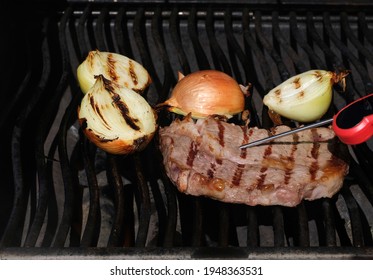 Testing steak temperature with meat thermometer on outdoor barbecue grill. Cut onions grilling