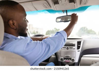 Testing Visibility. Happy Black Guy Adjusting Rear View Mirror, Enjoying New Auto, Sitting On Driver's Seat In Luxury Vehicle. Man Driving Alone, Over Shoulder View From The Back Passenger Seat