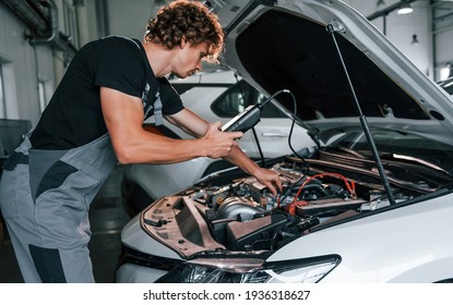 Tests car's electronics. Adult man in grey colored uniform works in the automobile salon.