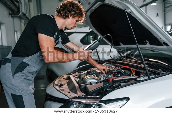 Tests car\'s electronics. Adult man in\
grey colored uniform works in the automobile\
salon.