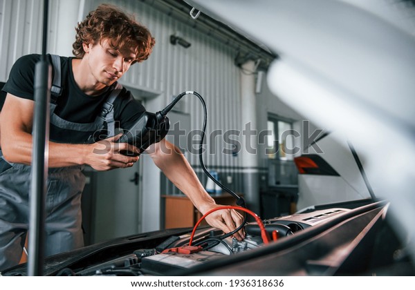 Tests car\'s electronics. Adult man in\
grey colored uniform works in the automobile\
salon.