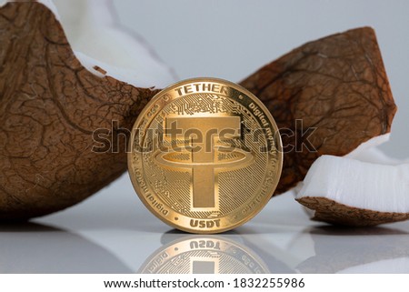Tether USDT cryptocurrency physical coin placed next to broken coconut on the white reflective table. Macro Shot.