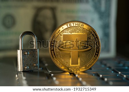 Tether USDT cryptocurrency physical coin placed on computer keyboard and small lock next to it.
