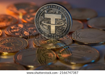 Tether USDT Cryptocurrency Physical Coin placed on crypto altcoins and lit with orange and blue lights in the dark Backgrond. Macro shot. Selective focus.