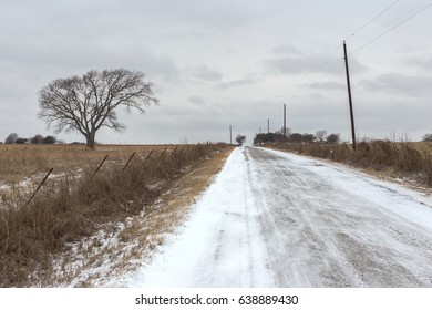 A Texas Country Road Covered In Ice And Snow Extends Into The Distance Past A Tree In A Field On A Bad Weather Day