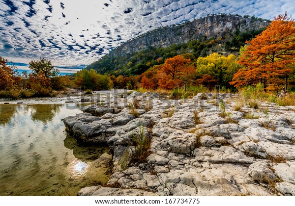 A Texas\
Hill Country Hill in the Background with Beautiful Fall Foliage\
Surrounding the Clear Frio River,\
Texas.