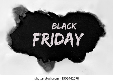 Text "Black Friday Sale" in burnt hole in white paper with burned edges, flat lay on black paper
