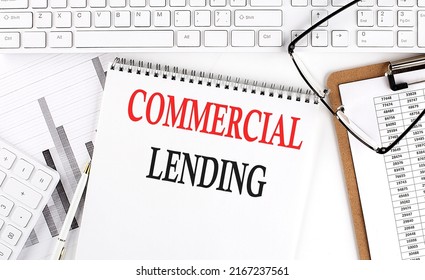 Text COMMERCIAL LENDING on Office desk table with keyboard, notepad and analysis chart on a white background.