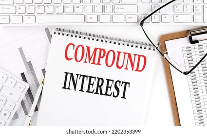 Text COMPOUND INTEREST On A Office Desk Table With Keyboard, Notepad And Analysis Chart On White Background.