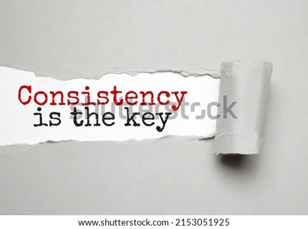 The text Consistency is the key appearing behind torn yellow paper