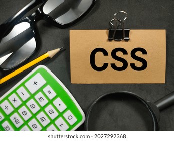 Text CSS (Cascading Style Sheet) writing on brown card with magnifying glass, pencil,calculator and glasses on black background.