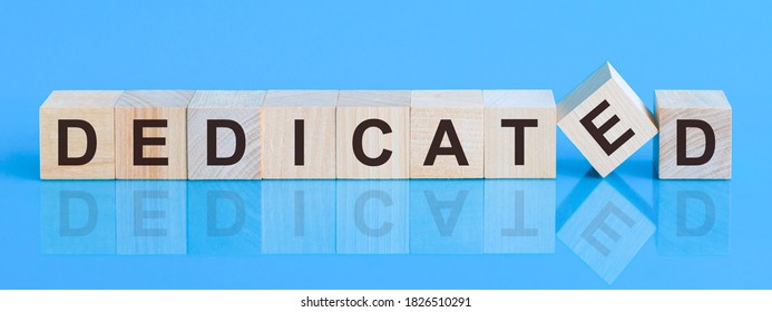 Text DEDICATED on wood cube block, stock investment concept. The text DEDICATED is written on the cubes in black letters, the cubes are located on a blue glass surface.