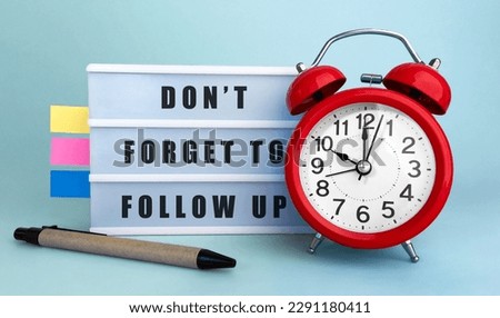 Text DONT FORGET TO FOLLOW UP written on the lightbox with alarm clock and colorfull stickers on blue background