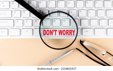 Text DON'T WORRY on keyboard with magnifier , glasses and pen on a beige background
