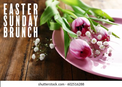 Text EASTER SUNDAY BRUNCH On Background. Plate And Flowers On Wooden Table