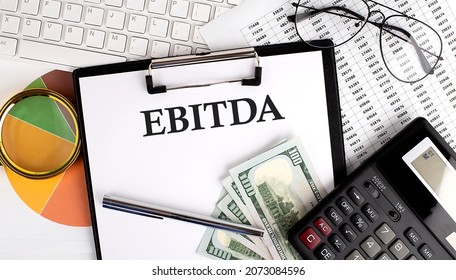 Text EBITDA on Office desk table with keyboard, dollars,calculator ,supplies,analysis chart on white background.
