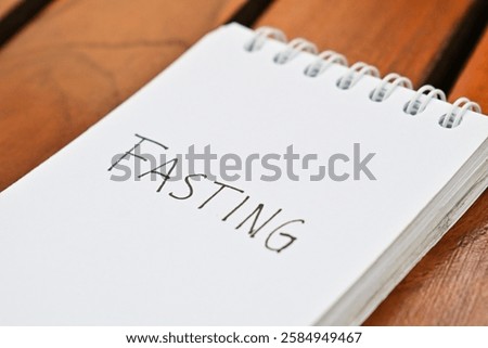 Text "Fasting" write by pen on a note book. wooden table background. Ramadan concept. Close up view.