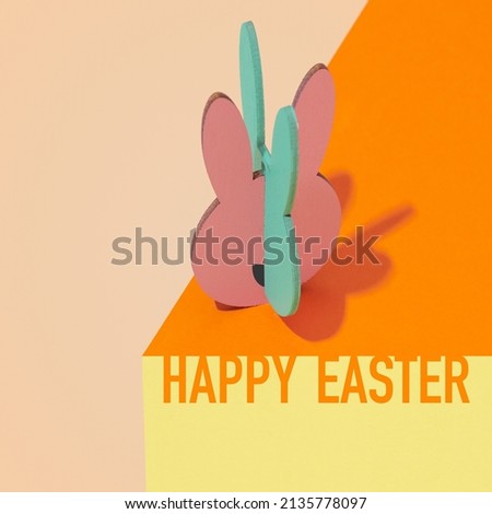 text happy easter and an easter bunny cut out on thin plywood painted in different colors, on an orange, yewllo and pale brown surface creating a visual illusion
