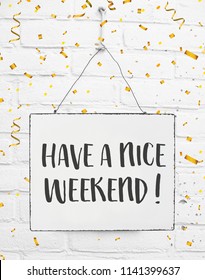 Text have a nice weekend white sign banner board with golden confetti on white brick background