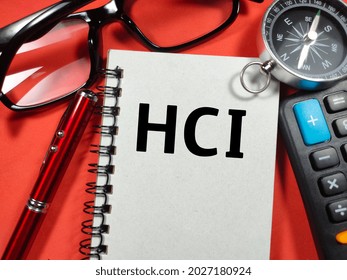 Text HCI (Human Computer Interface) writing on notebook with compass,pen,calculator and glasses on red background.