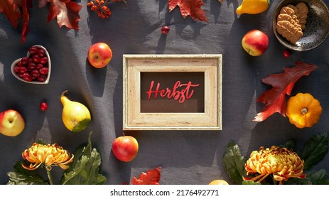Text Herbst means Autumn in German language. Blackboard, frame and Autumn decor. Chrysanthemum flowers, bunny tail grass and red oak leaves, pumpkins, cranberry. Fall decor, flat lay on dark textile.