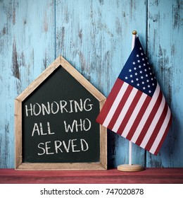 the text honoring all who served written in a house-shaped chalkboard and a flag of the United States, against a blue rustic wooden background