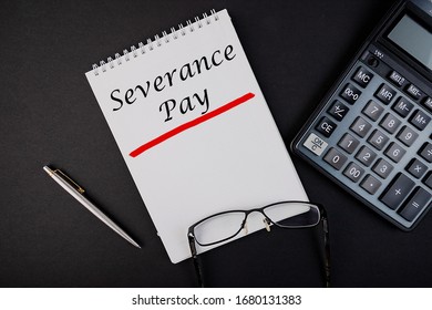 Text, the inscription, the phrase Severance Pay is written in a notebook that lies on a dark table with a calculator and pen and glasses. Business concept.