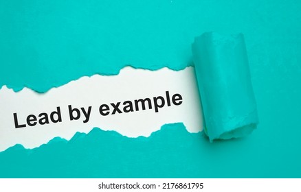 The text lead by example appearing behind torn grey paper