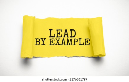 The text lead by example appearing behind torn grey paper
