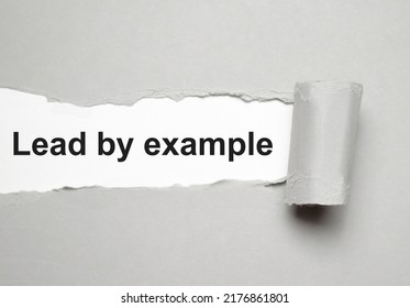 The text lead by example appearing behind torn grey paper
