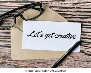 Text Lets Get Creative Written On White Paper With A Pen,brown Envelope And Eye Glasses.