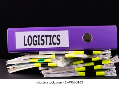 Text LOGISTICS is written on a folder lying on a stack of papers on a table. Business concept