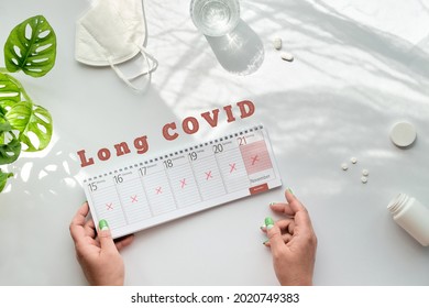 Text Long Covid, Patient Hands Hold Weekly Planner. German Text Means Days Of The Week. Cancellation, Change Of Plans Due To Chronic Covid Condition. Off White Table With Water, Mask, Pills.