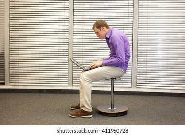 text neck - man in slouching position sitting on pneumatic stool, working with laptop in his office