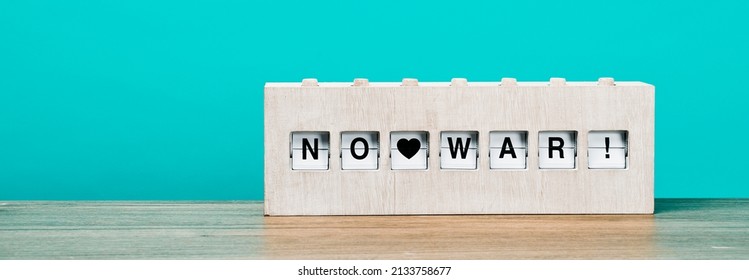 text no war written in a rustic wooden split flap display, on a wooden surface against a blue background, in a panoramic format to use as web banner or header