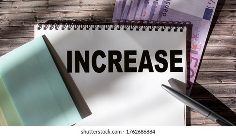 Text on a white sheet. Increase Income. On a wooden table is the euro. Currency, stickers and pen. The concept of an increase in a company is sales from one period to another.
