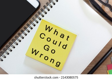 Text on yellow note with notepad on wooden desk - What could go wrong. Business and audit concept