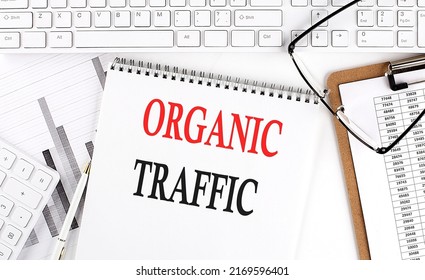 Text ORGANIC TRAFFIC On Office Desk Table With Keyboard, Notepad And Analysis Chart On A White Background.