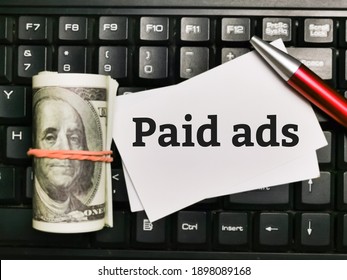 Text PAID ADS written on white paper note with pen and fake money on computer keyboard.Business concept.