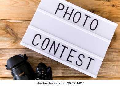 Text "photo contest"  written on white slate with camera on wooden background. Suitable for advertising