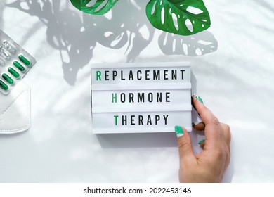 Text Replacement Hormone Therapy On Light Box In Hand. Menopause, RHT Therapy Concept. Estrogen Replacement Therapy Awareness Design. Off White Background With Monstera Leaves. Flat Lay, Top View.