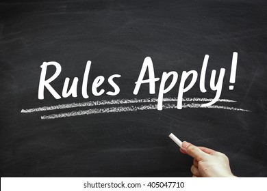 Text Rules Apply written on the blackboard with hand holding white chalk aside.
