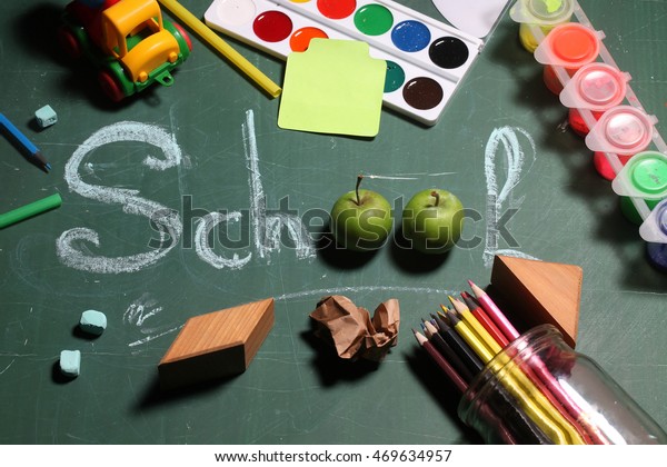 Text school word in centre\
drawing with chalk and apples surrounded by stationery colorful\
paints colored pencils wooden blocks note paper on green chalkboard\
background