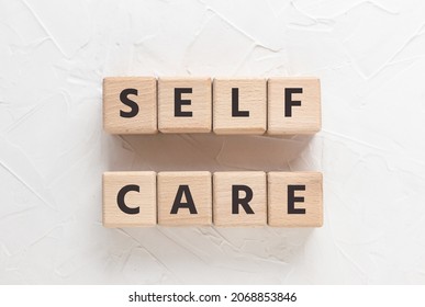 Text SELF CARE on wooden cubes on white textured putty background. Square wood blocks. Top view, flat lay.