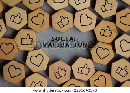 Text SOCIAL VALIDATION surrounded by wooden cubes with thumbs up and heart icon. Social validation concept