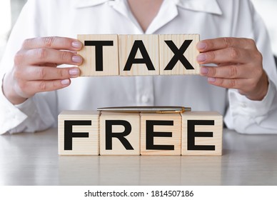 Text tax free on wooden blocks on a wooden table. Hands of businesswoman as the background. Financial concept.