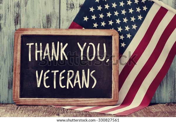 the text\
thank you veterans written in a chalkboard and a flag of the United\
States, on a rustic wooden\
background