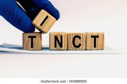 Text TINCT made from wooden cubes. Hands in a blue glove. - Shutterstock ID 1950800005